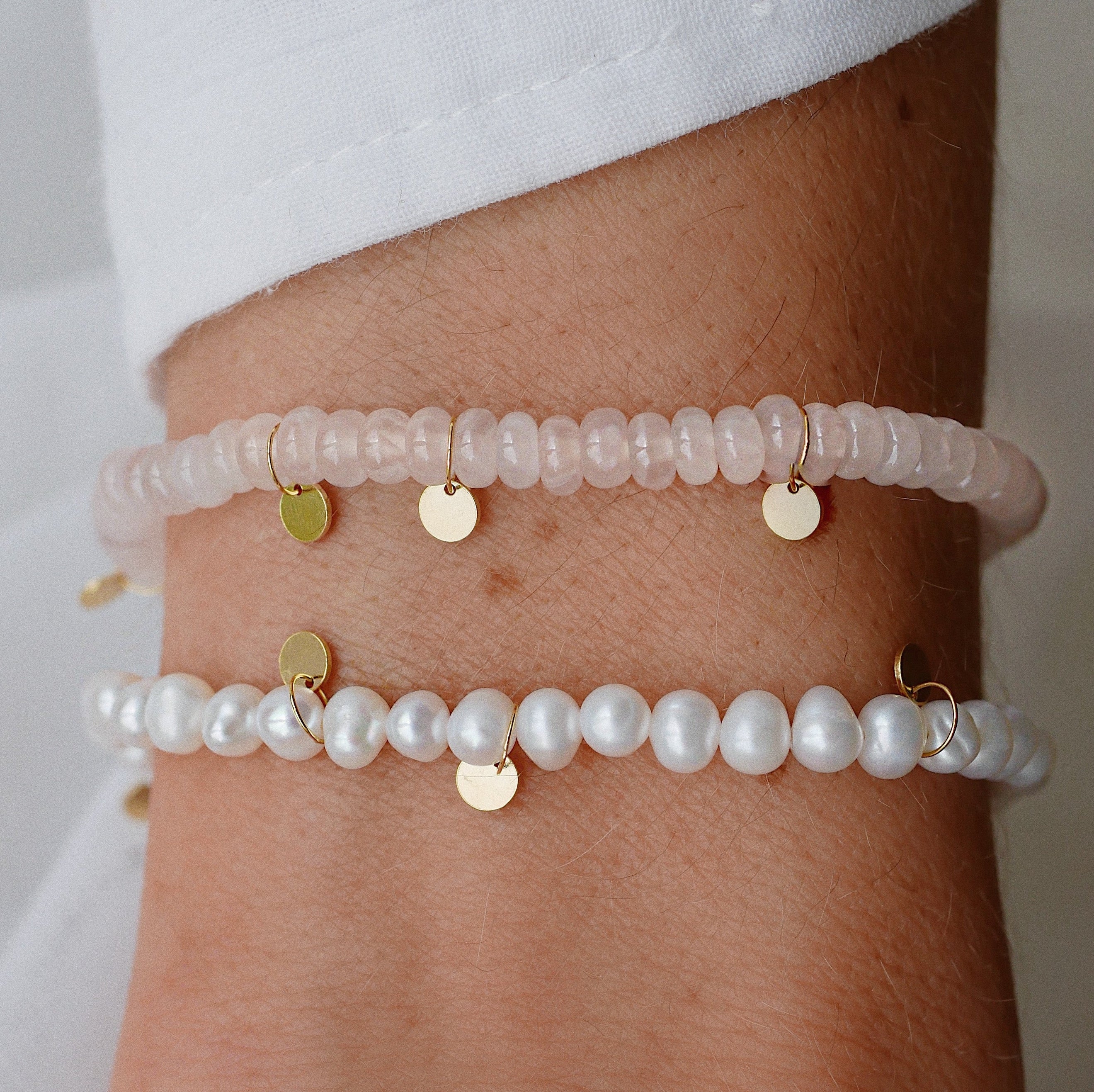 Two pearl bracelets with gold accents on a wrist against a white background