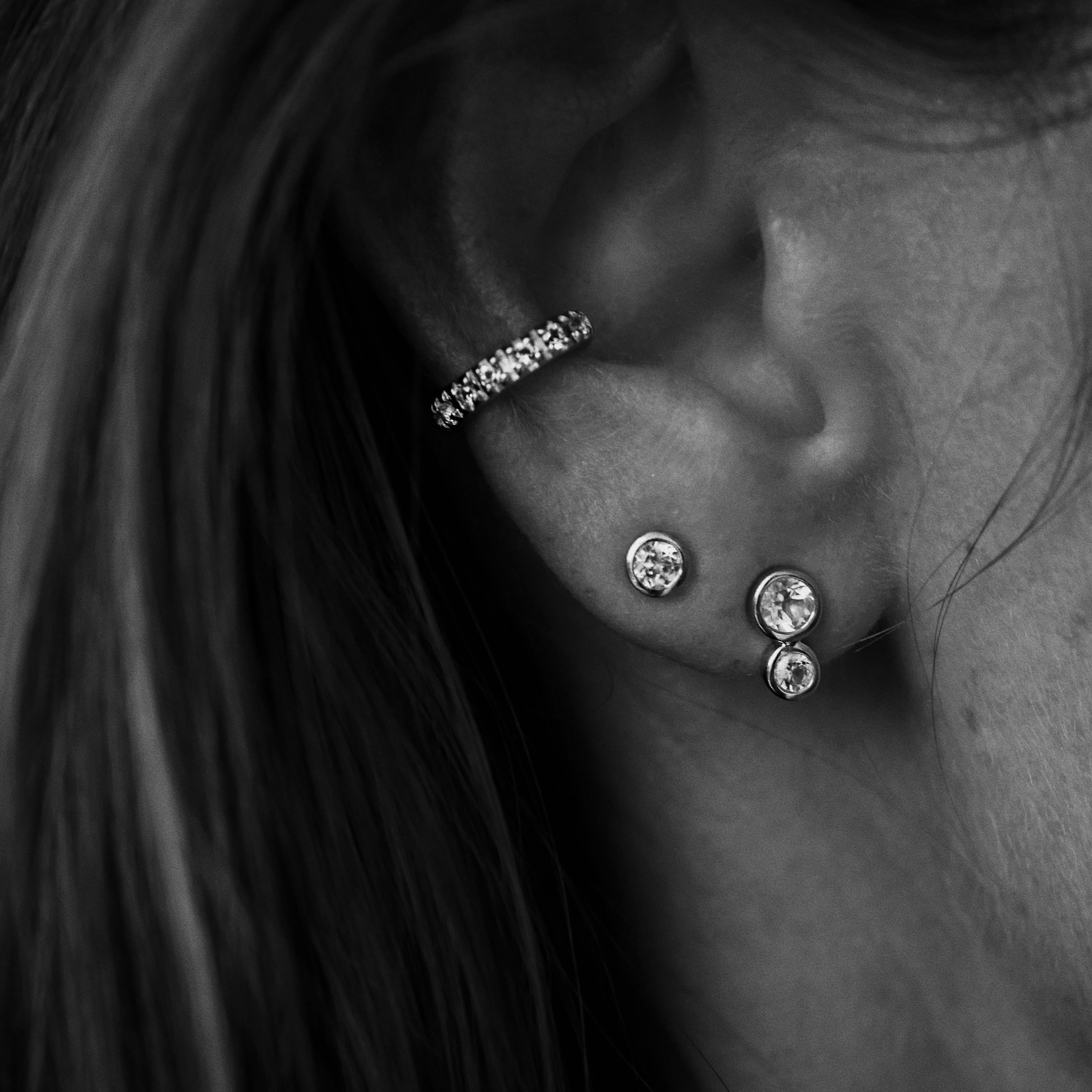 Close-up of an ear with multiple earrings in black and white