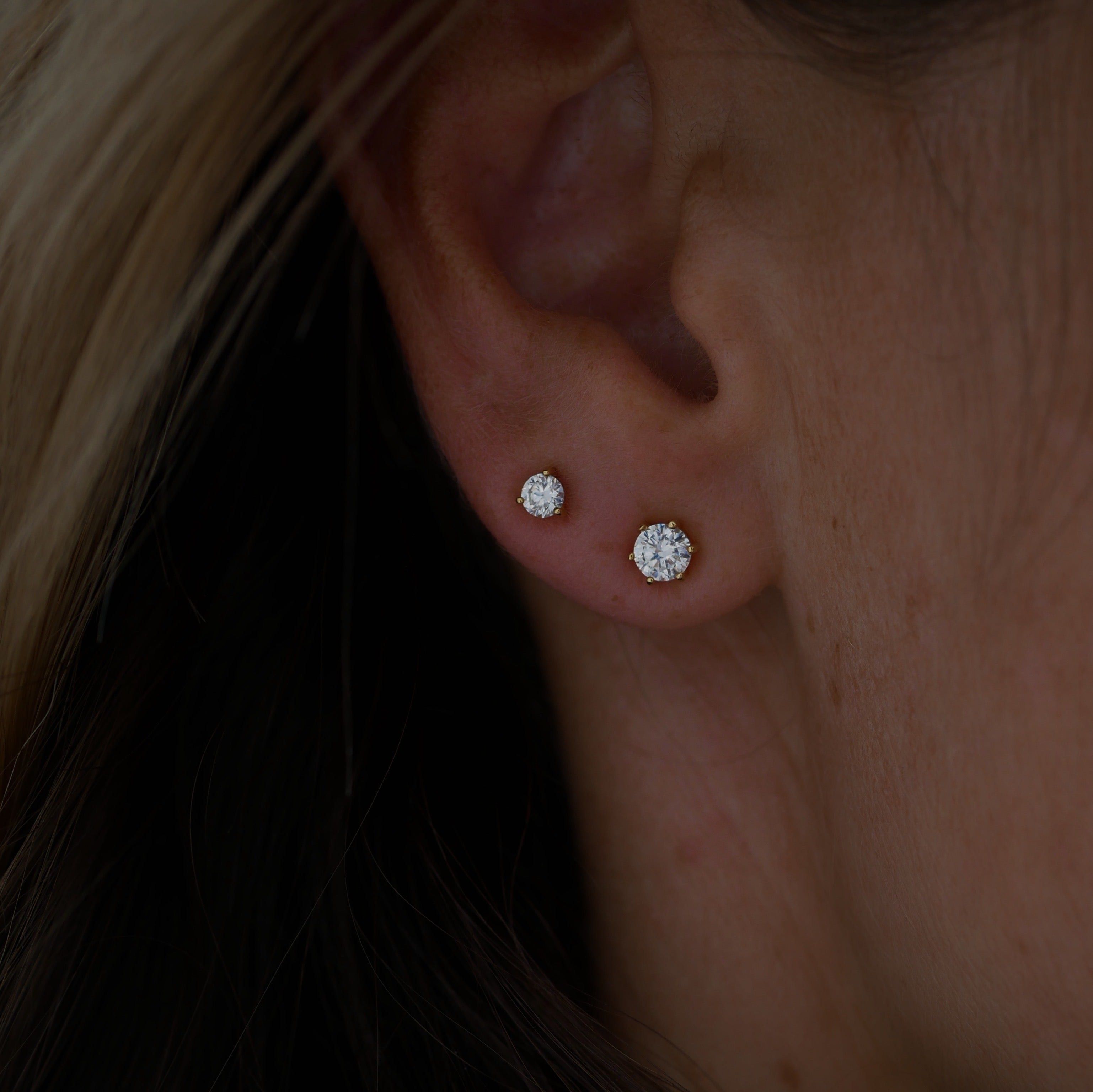 Close-up of an ear wearing two cubic zirconia stud earrings.