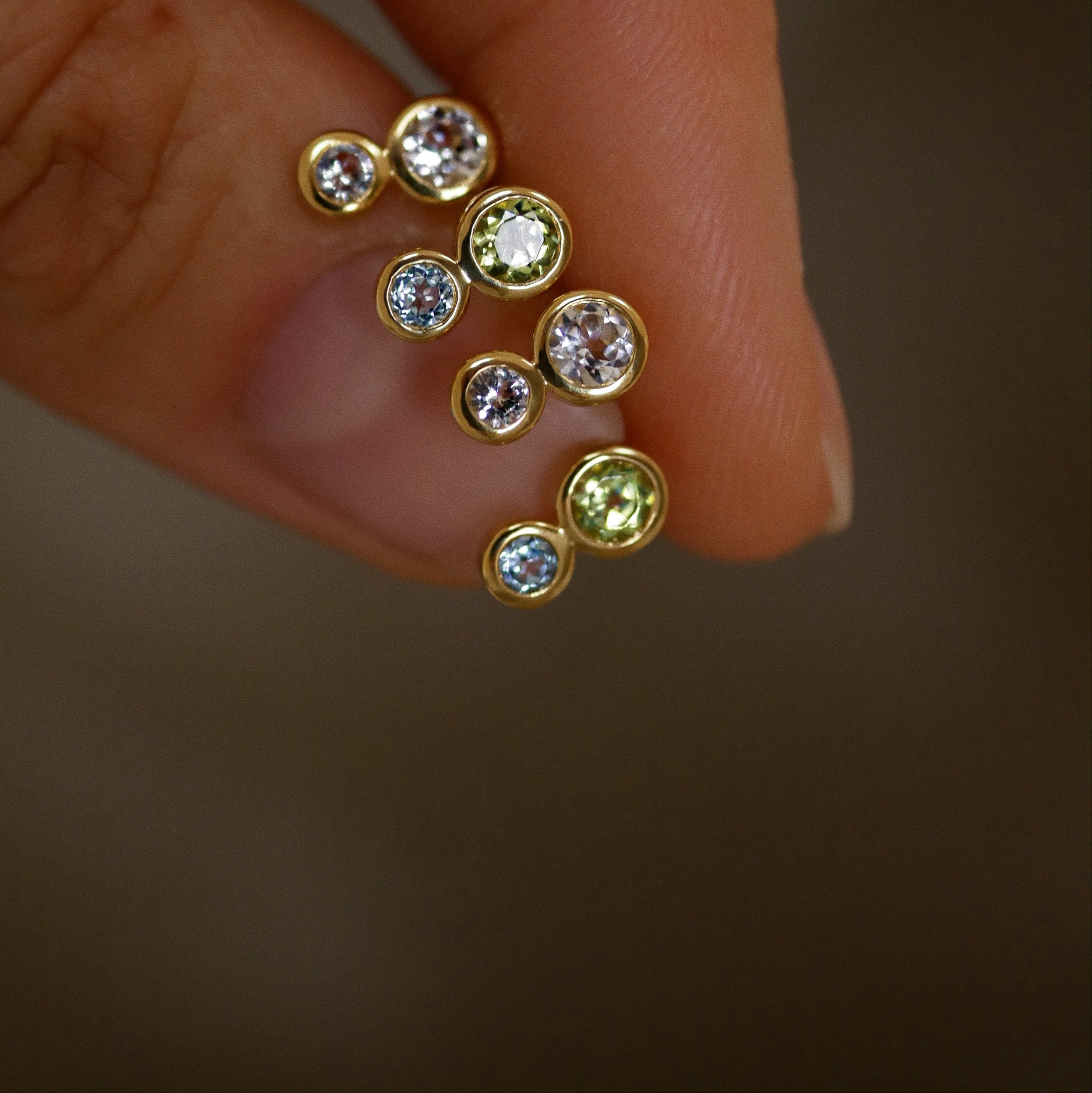 Gold earrings with gemstones held between fingers against a blurred background