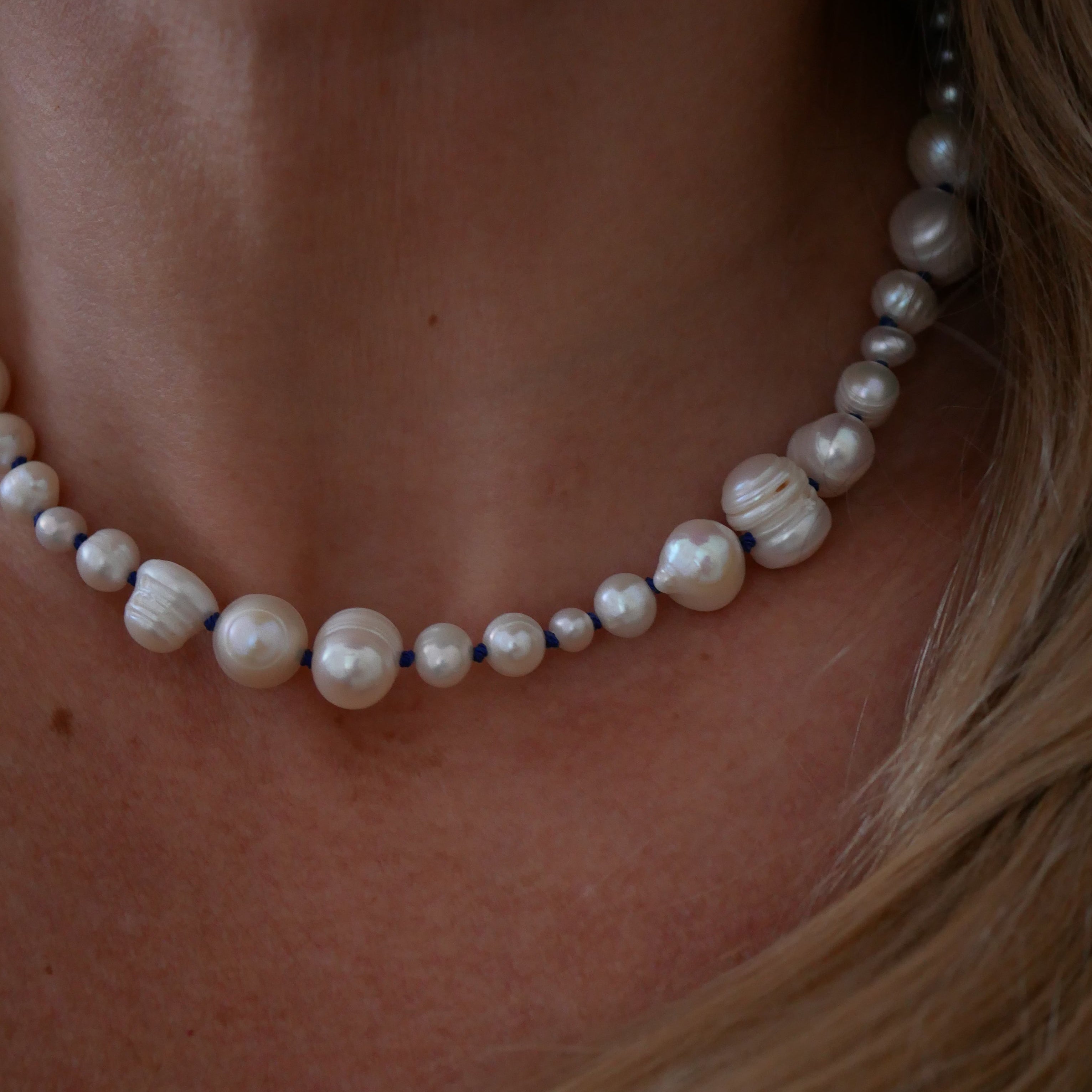 Pearl necklace draped over a person's neck with blonde hair.