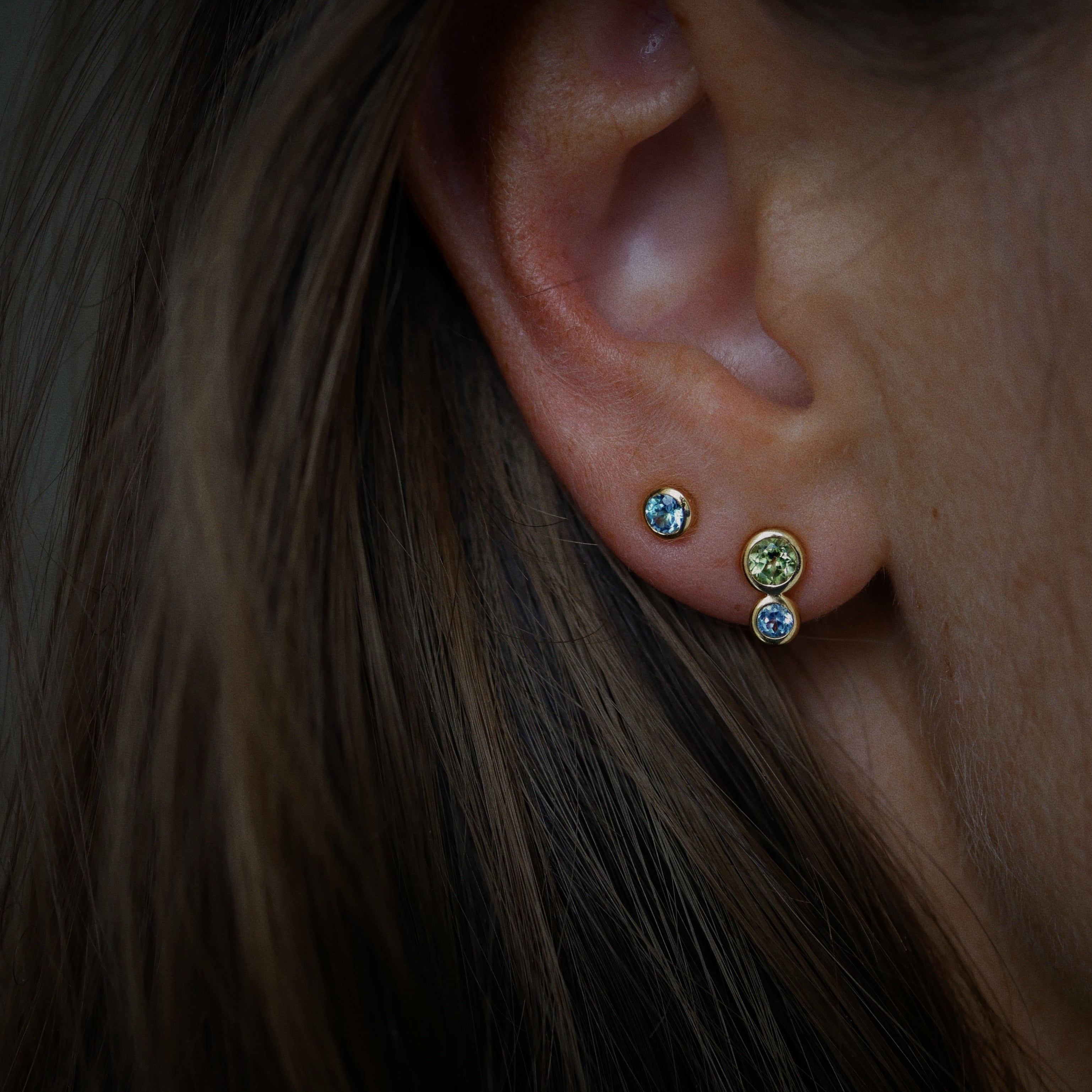 Close-up of an ear wearing a set of earrings with gemstones.