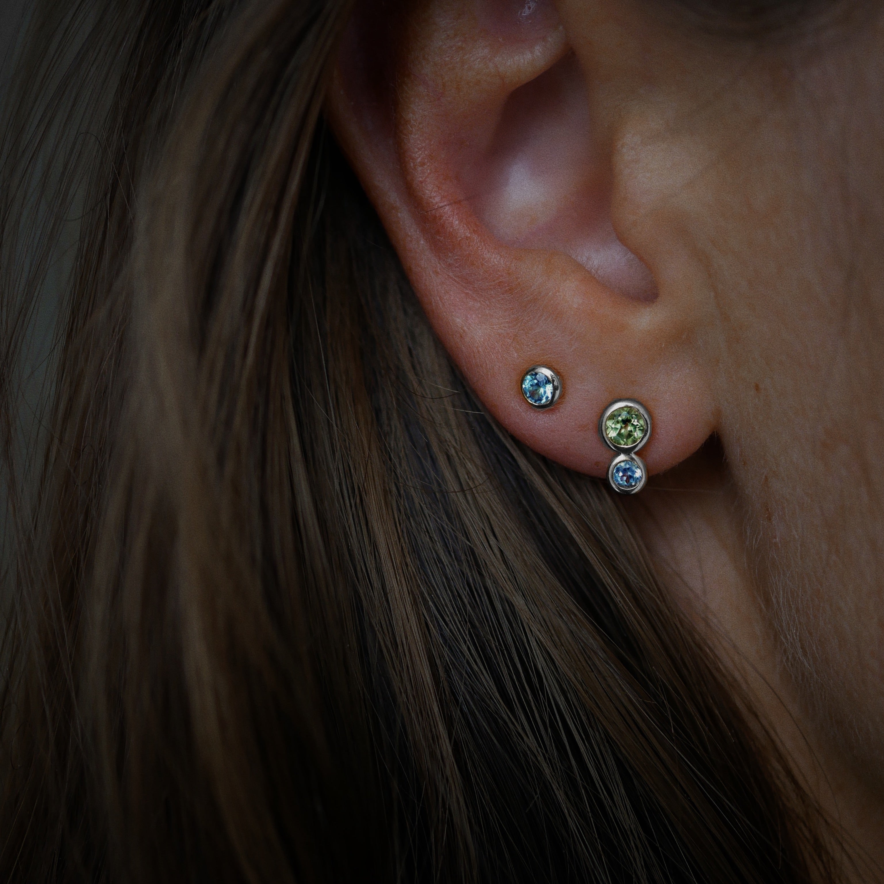 Close-up of an ear wearing multiple earrings with a dark background