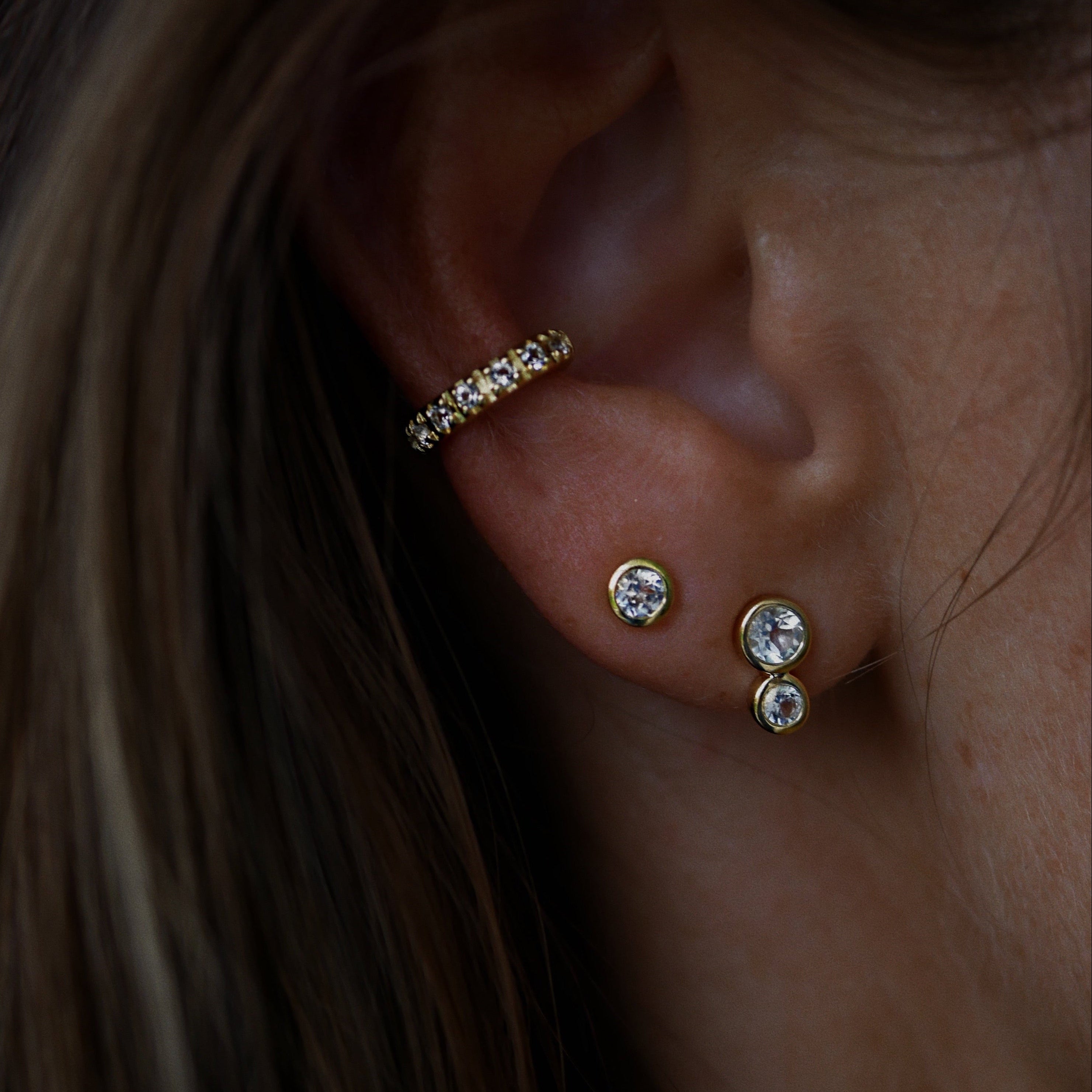 Close-up of an ear with gold and topaz earrings against a dark background