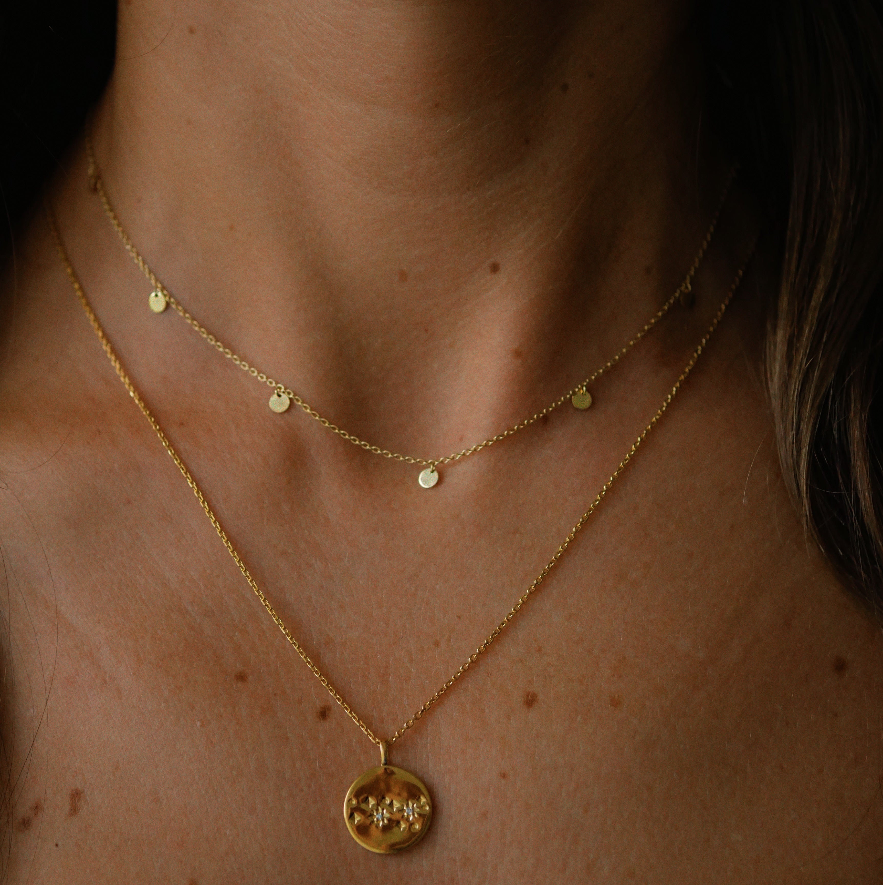 Close-up of a person wearing a gold necklace with a pendant on a dark background