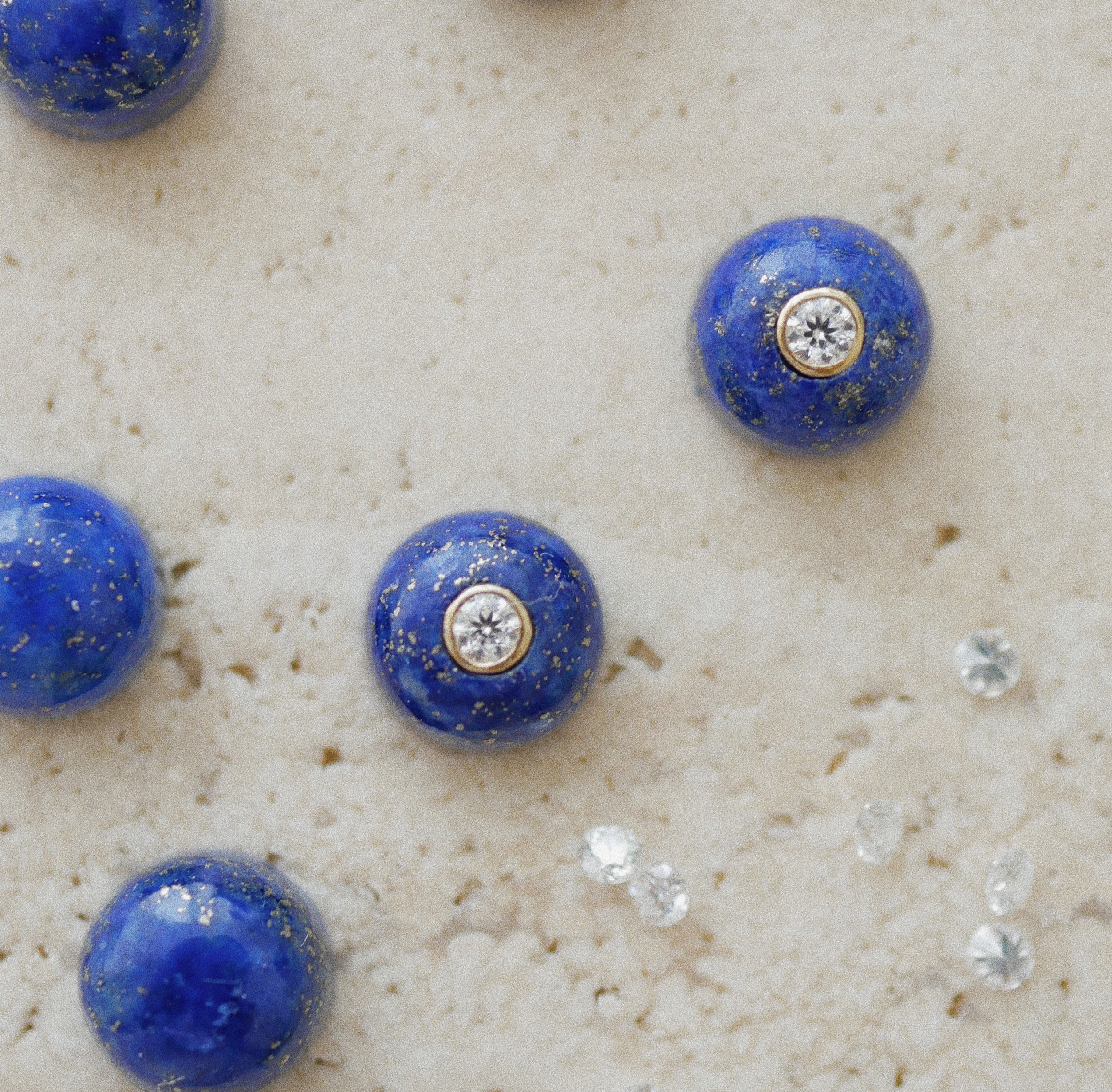 Blue gemstone earrings with embedded moissanites on a textured beige surface