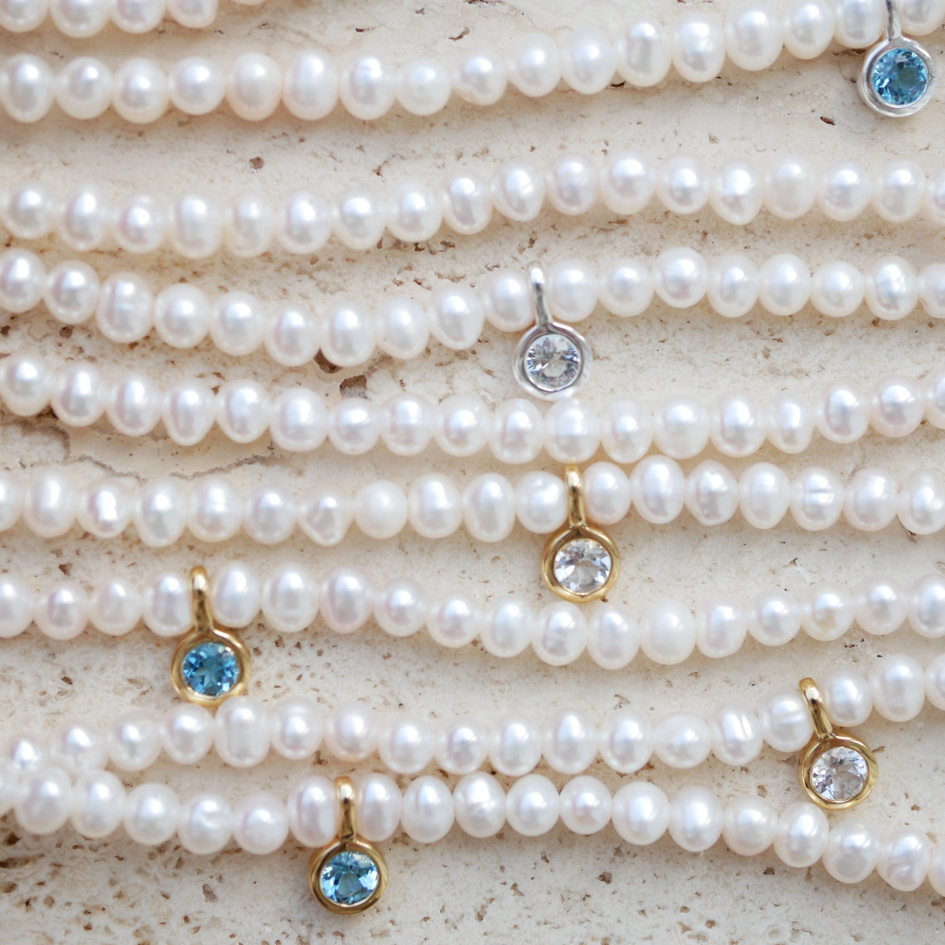 Multiple pearl necklaces with gemstone pendants on a textured surface