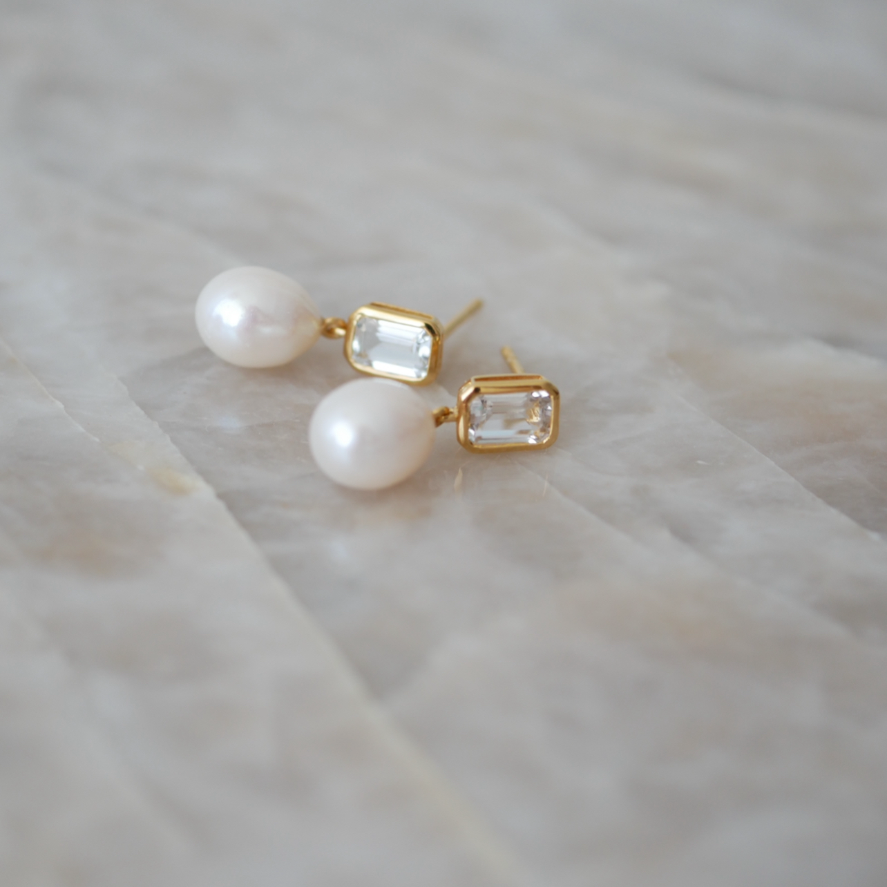 Pair of pearl earrings with gold accents on a light marble surface