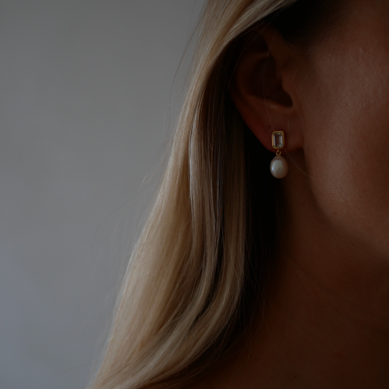 Close-up of a person wearing pearl earrings with a neutral background