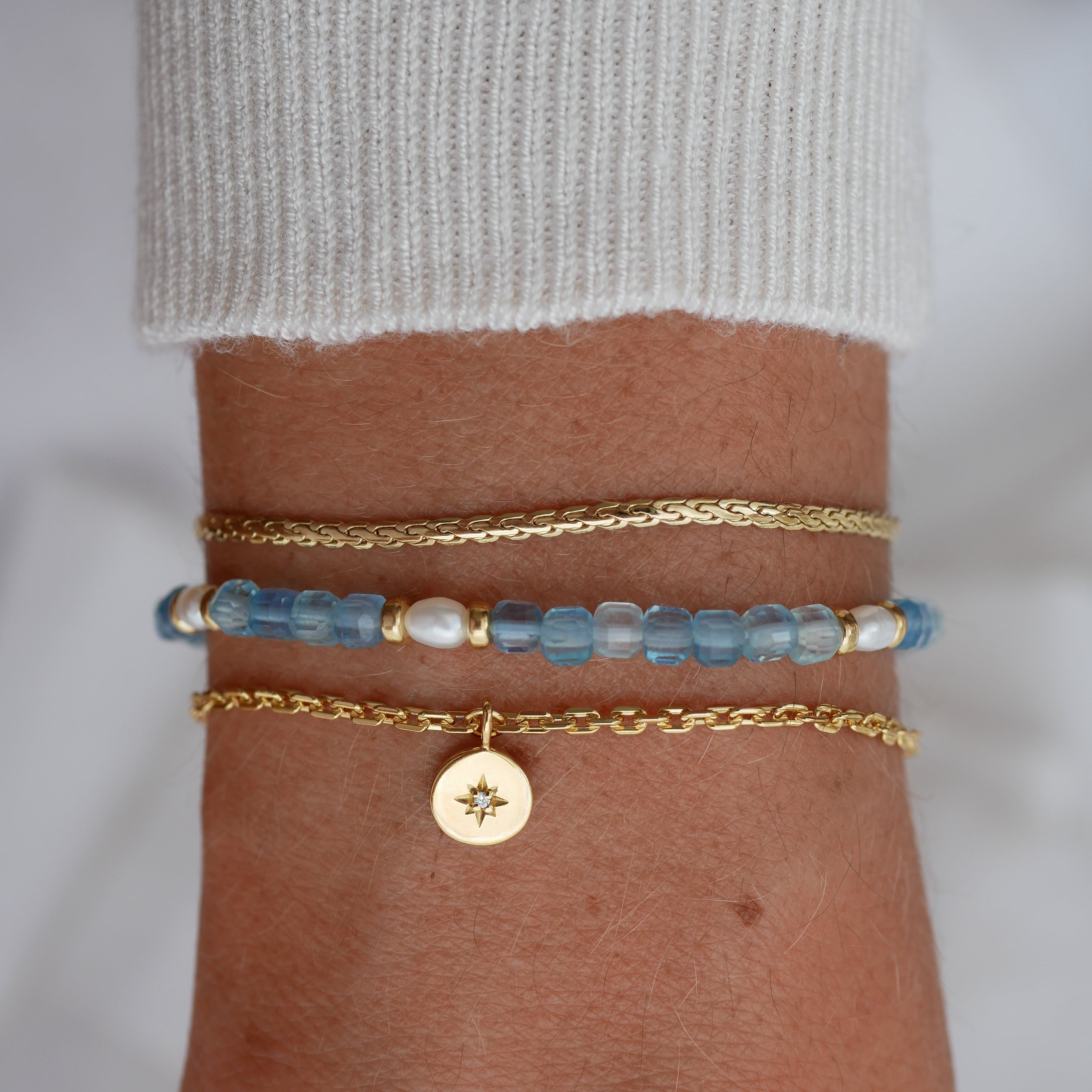 Close-up of a wrist wearing two bracelets with blue beads and gold accents on a neutral background.
