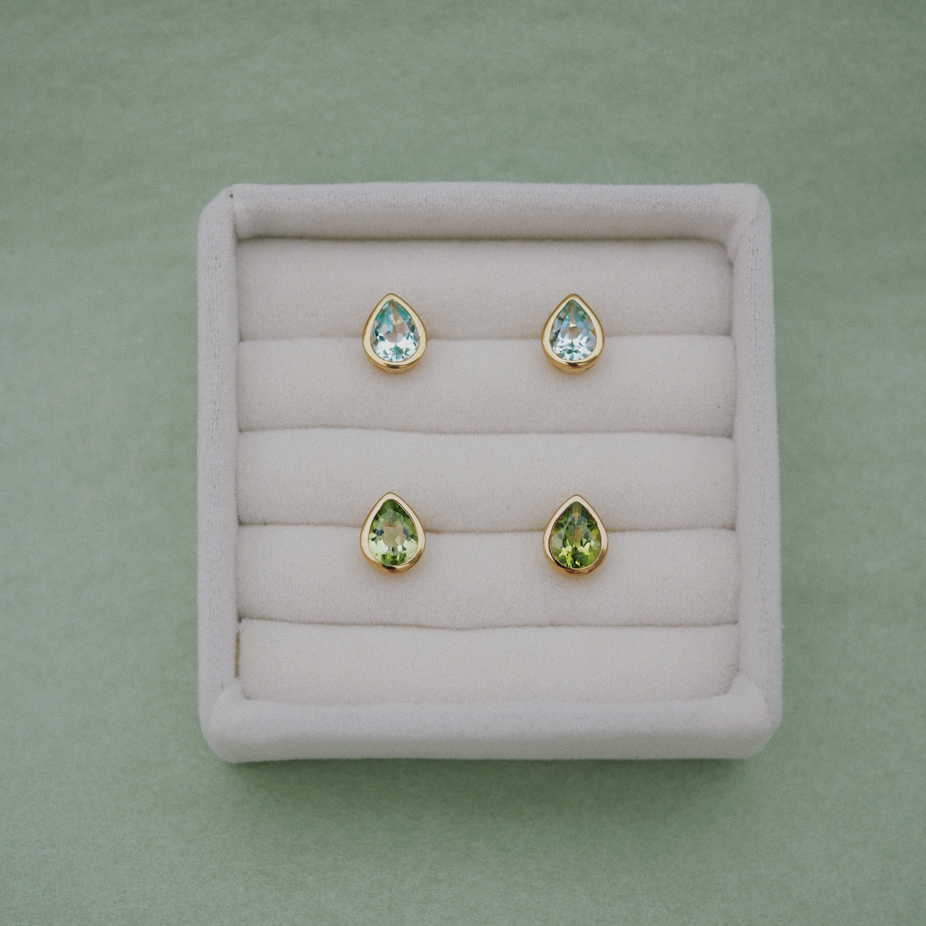 Set of green teardrop earrings on a display tray with a green background