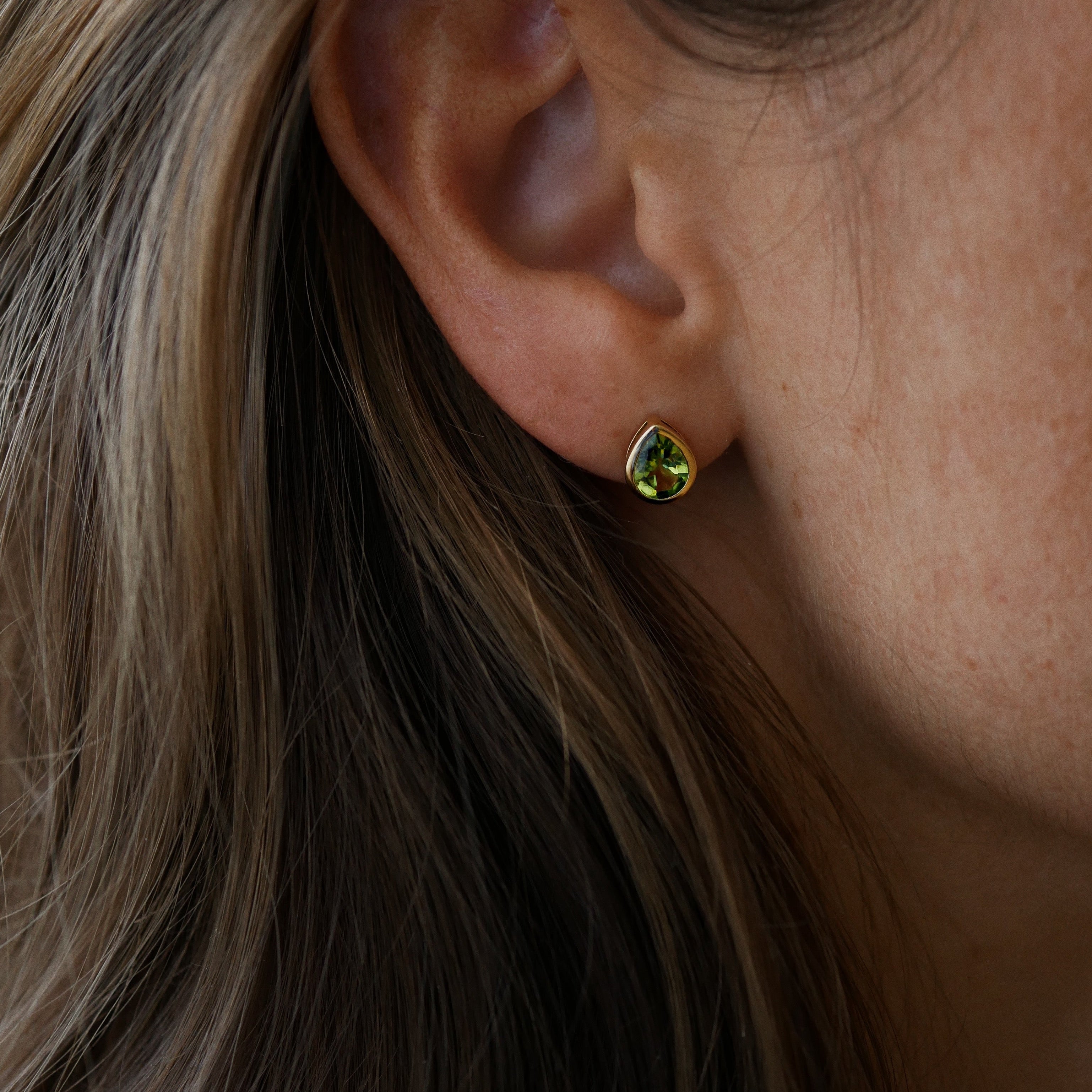 Close-up of an ear wearing a green gemstone earring with hair partially obscuring the view.