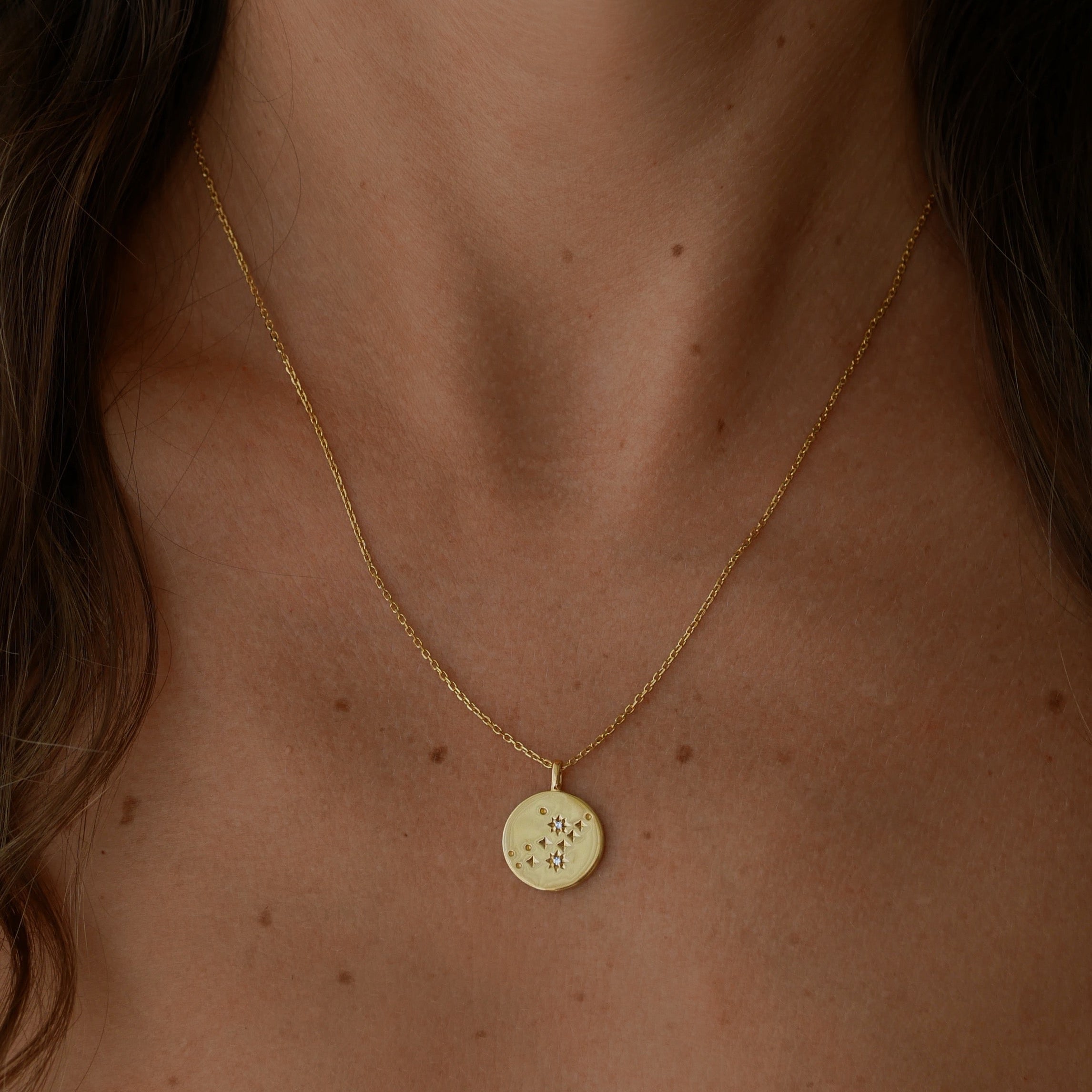 Gold necklace with a round pendant on a person's neck against a dark background