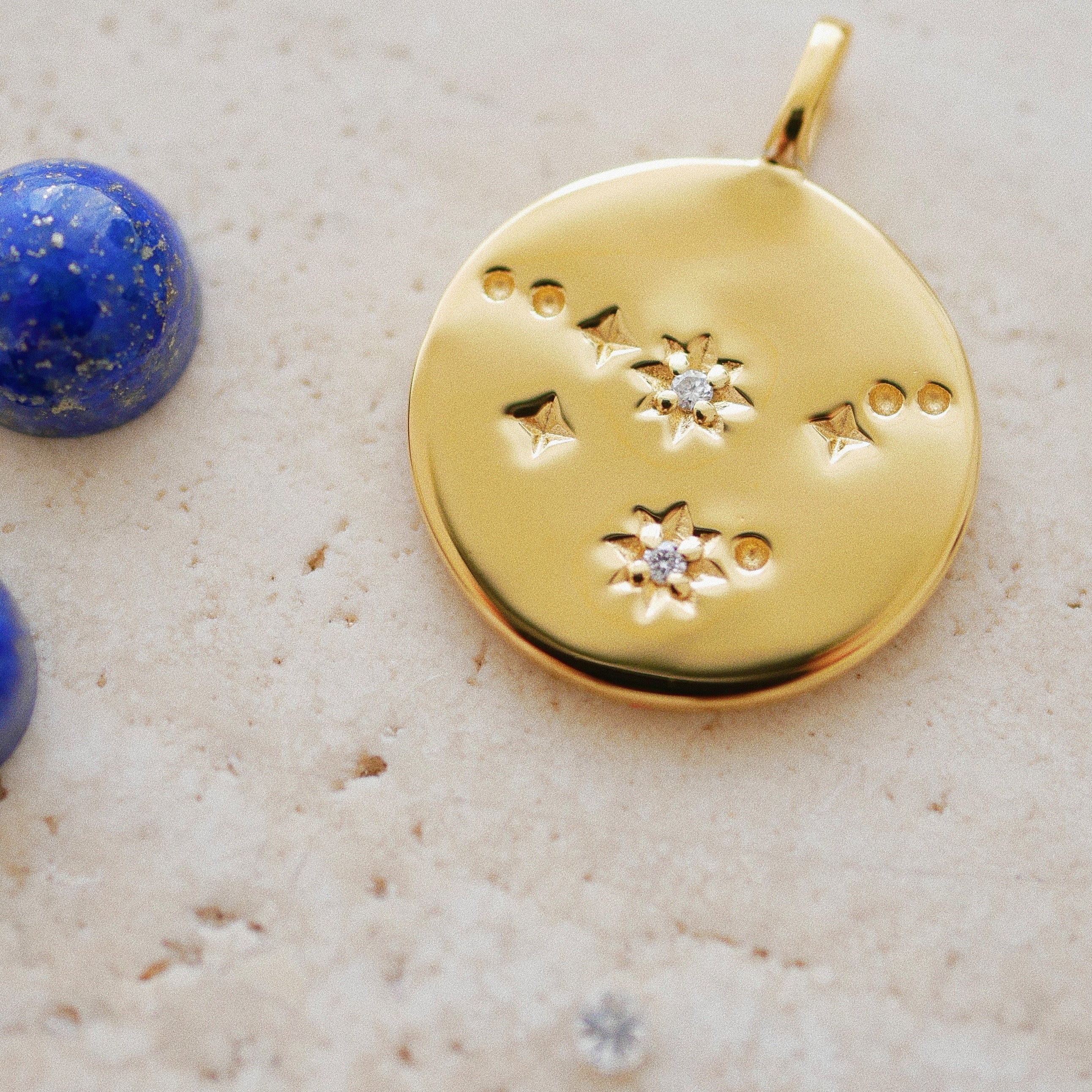 Gold pendant with star designs on a textured beige surface