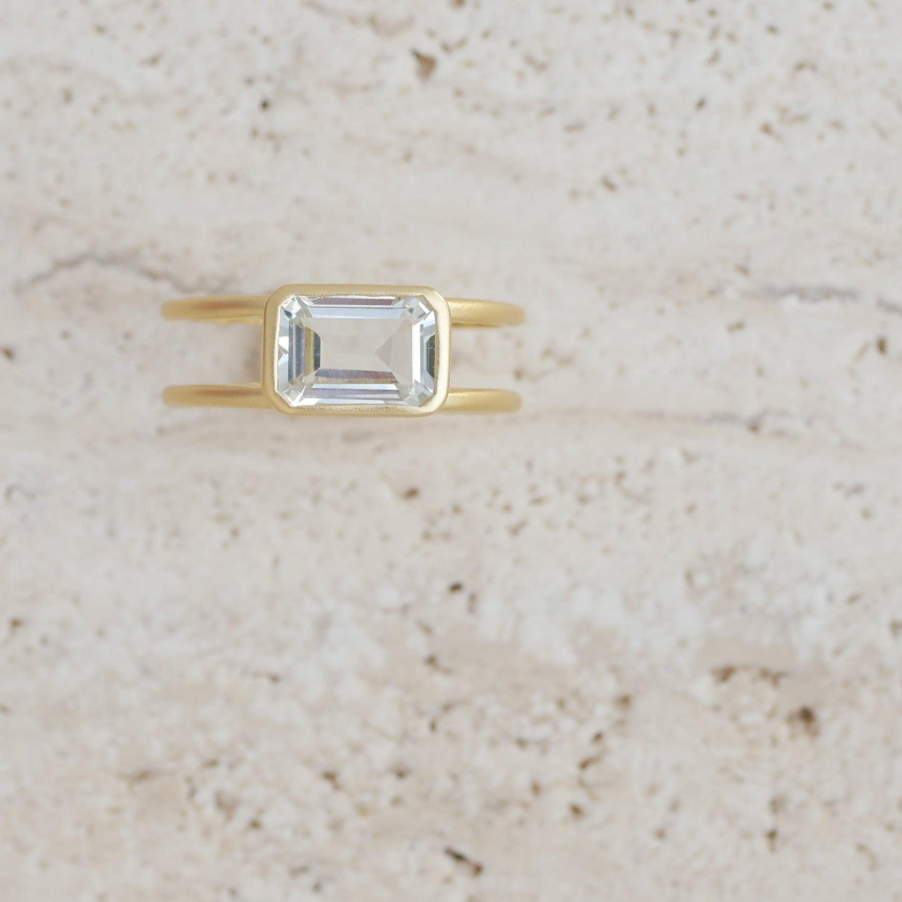 Gold ring with a rectangular gemstone on a beige surface