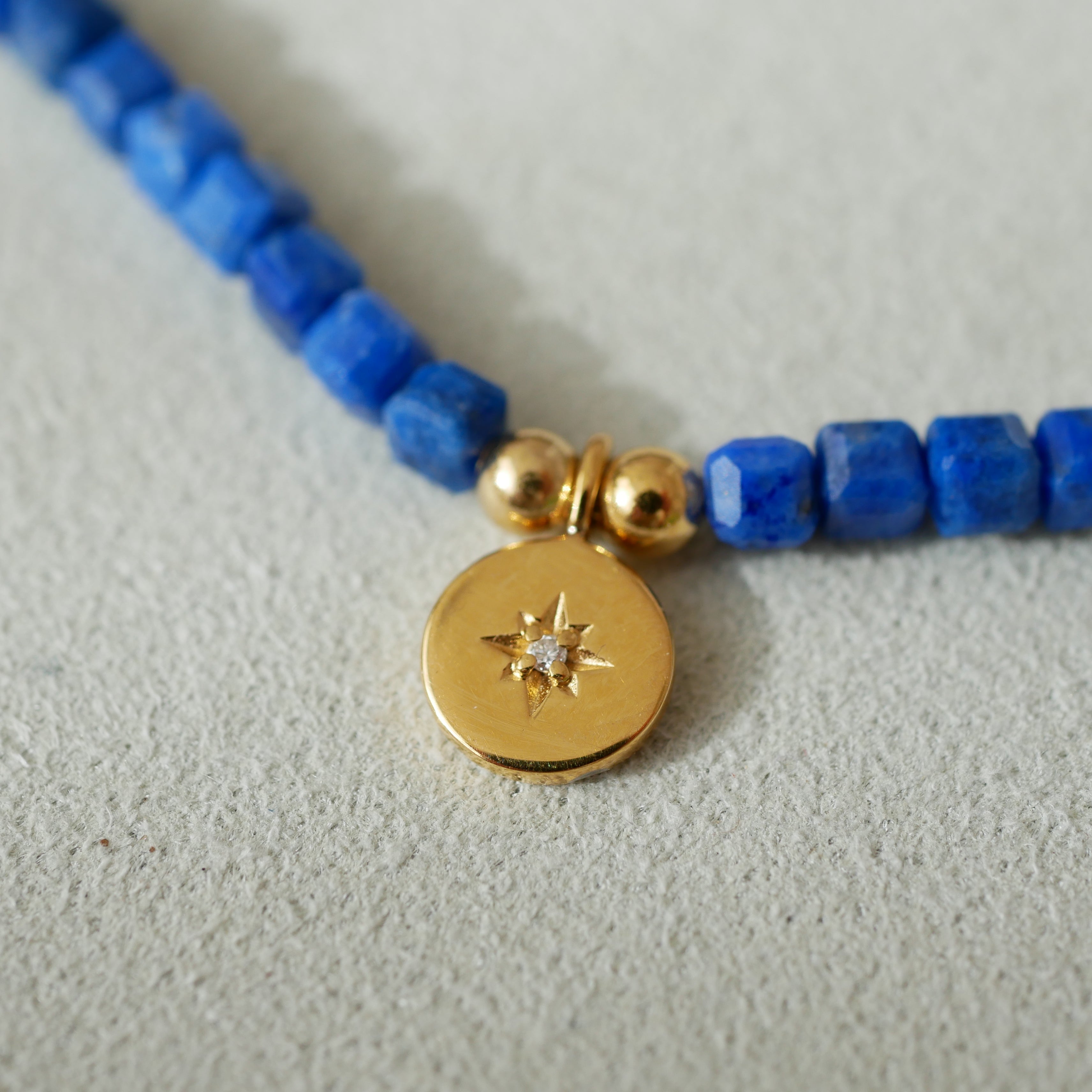 lapis lazuli beaded necklace with a gold charm featuring a star design on a light gray background
