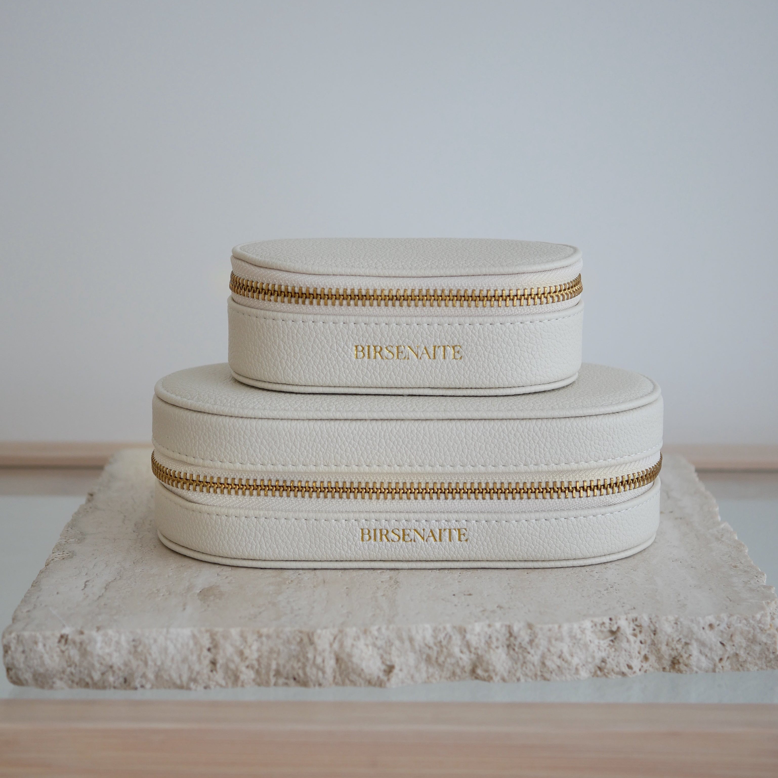 Two cream-colored jewelry boxes with gold zippers on a textured surface.