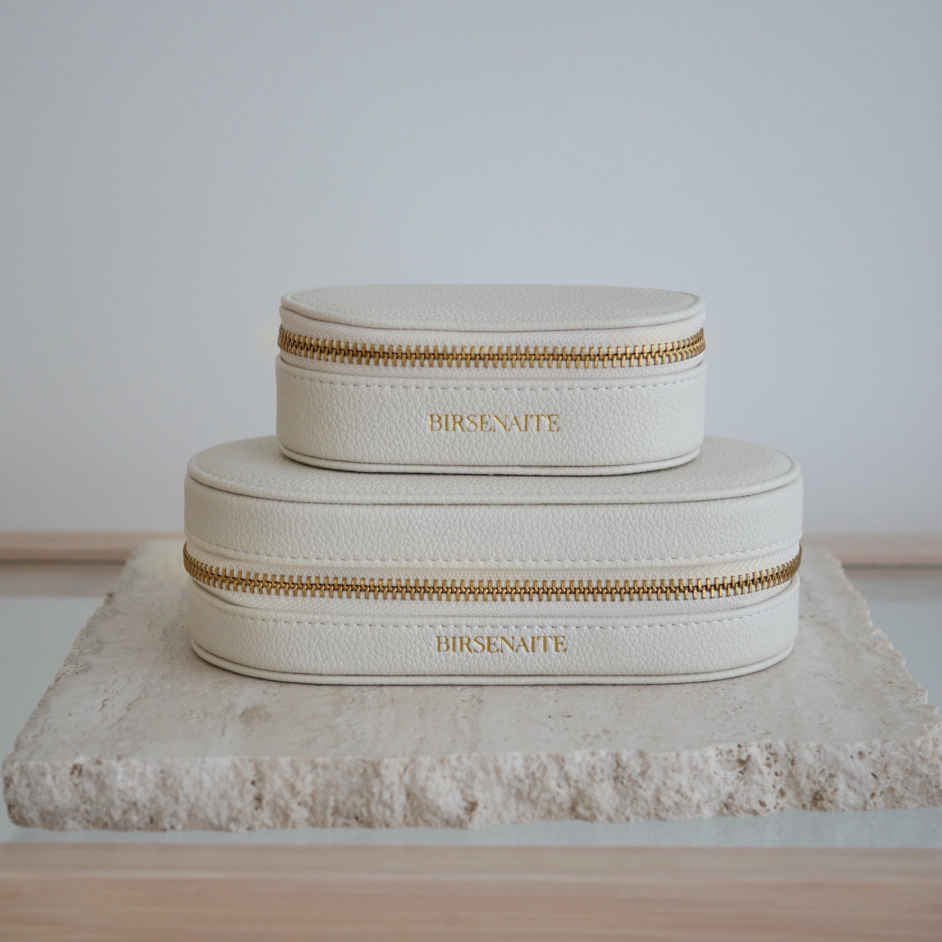 Two cream-colored jewelry boxes with gold zippers on a textured surface.