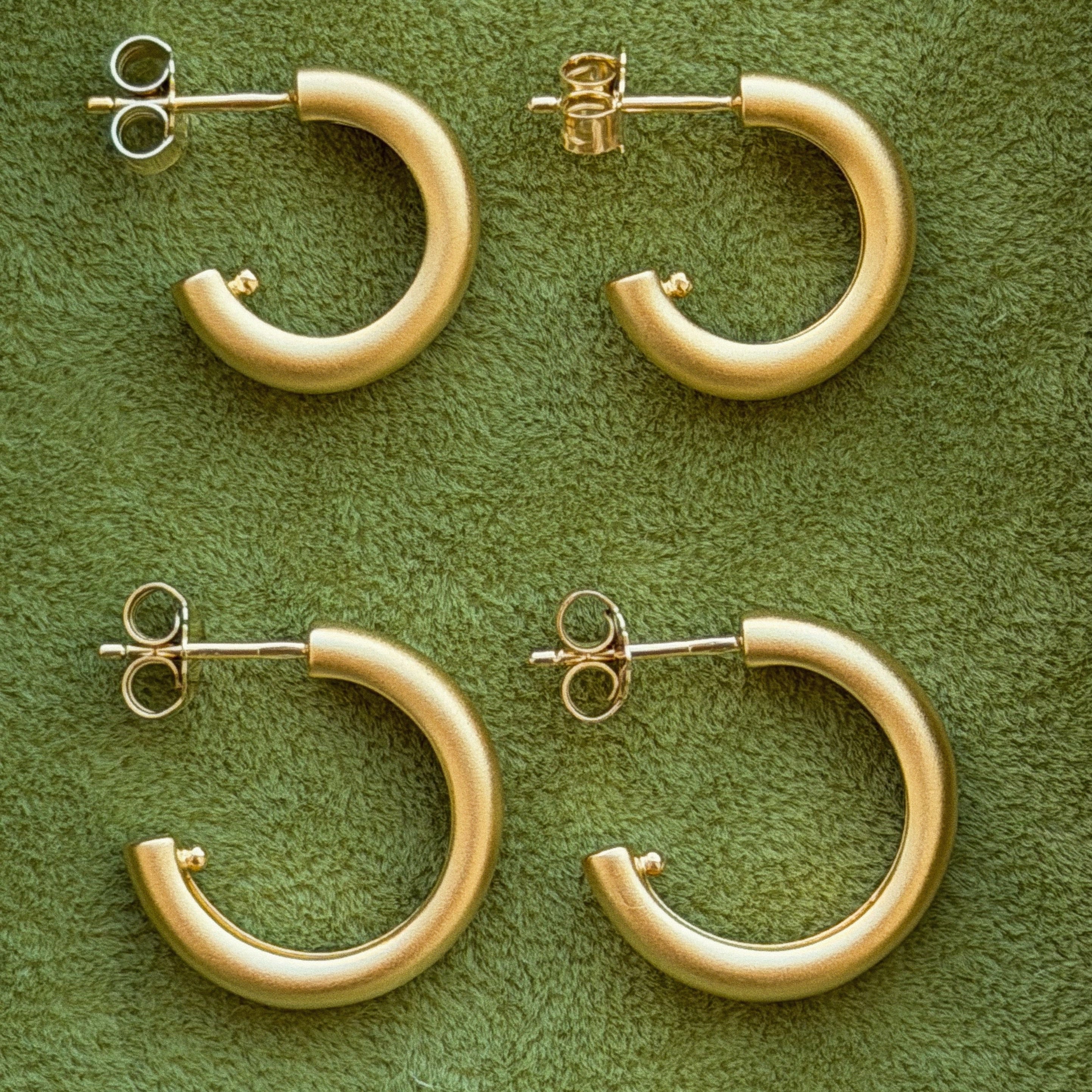 Gold hoop earrings on a green textured surface