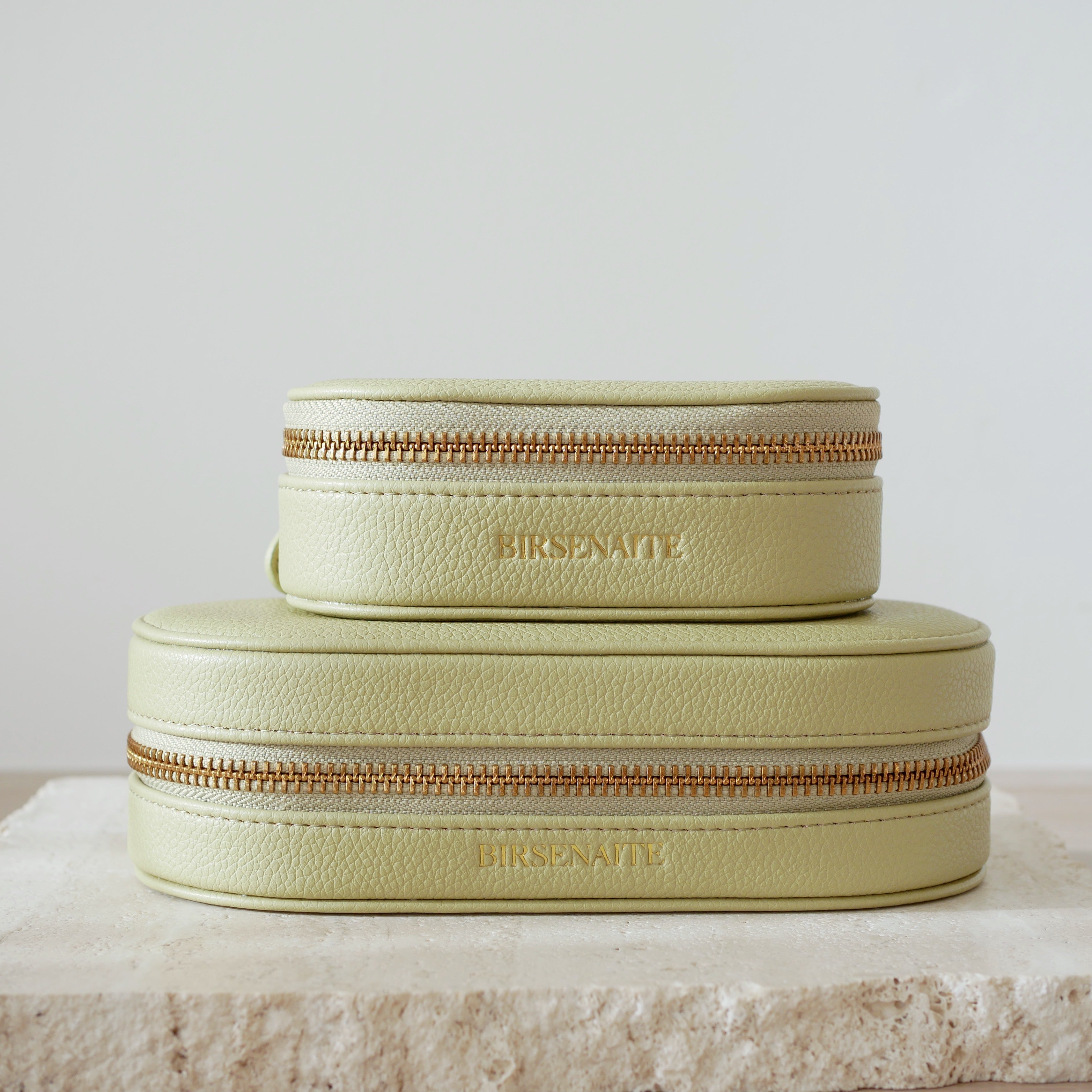 Two sage green jewelry boxes with gold zippers on a light gray background